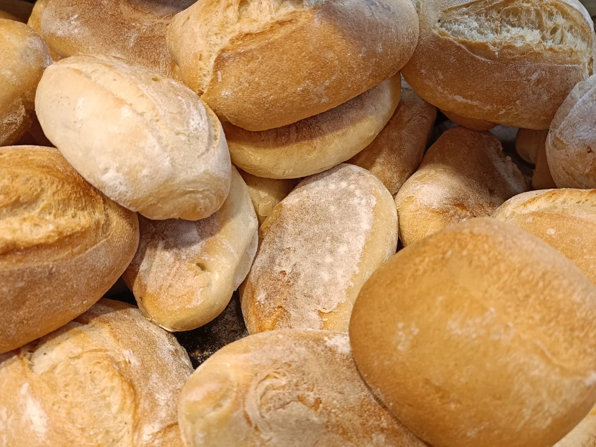 Viele helle, bemehlte Backwaren mit aufgerissener Kruste, dicht übereinander gehäuft.
