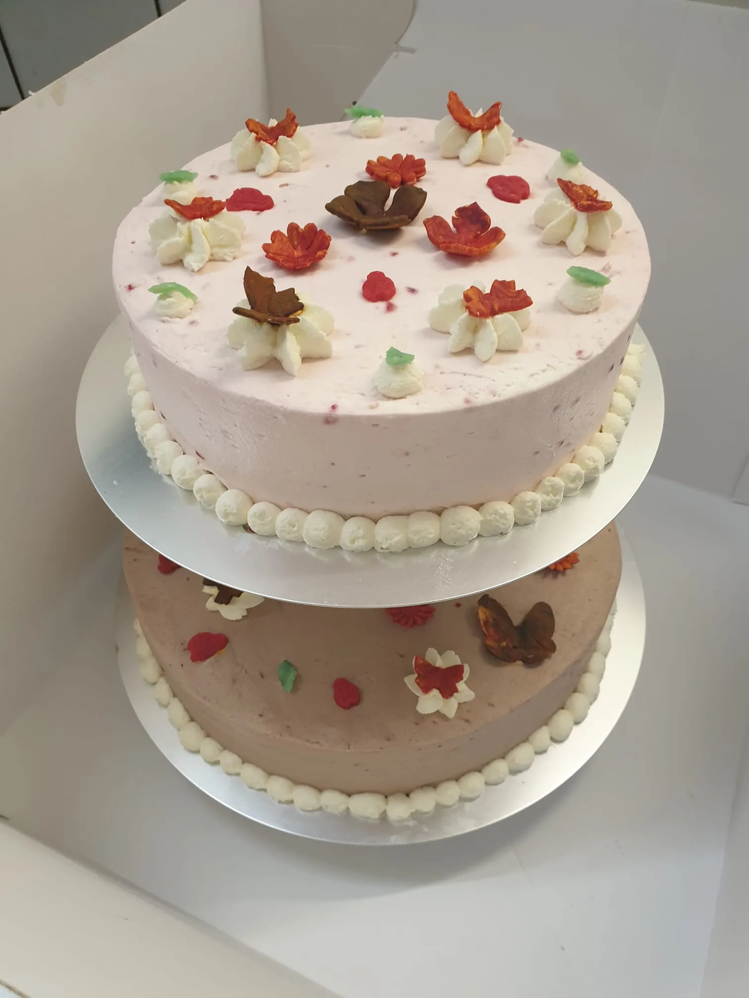 Eine zweistöckige rosa Torte mit Blüten aus Zuckermasse.