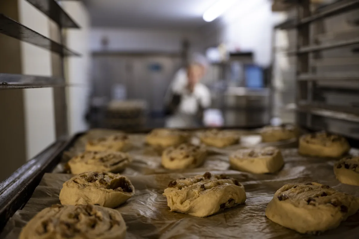 Rosinenbrötchen-Teiglinge auf dem Blech, dahinter die Backstube.