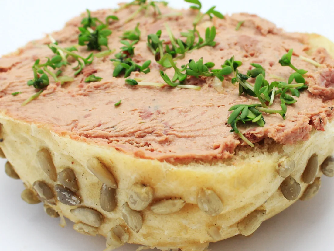 Eine Brötchenhälfte mit Kürbis- und Sonnenblumenkernen, mit Leberwurst bestrichen und mit Kresse bestreut.