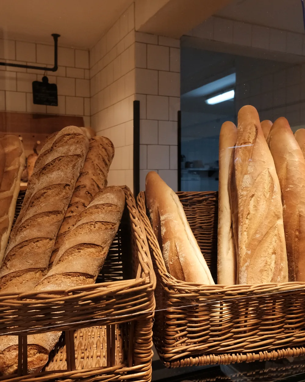Stangenbrote in zwei Weidenkörben, dahinter die weiß gefliesten Wände der Backstube.