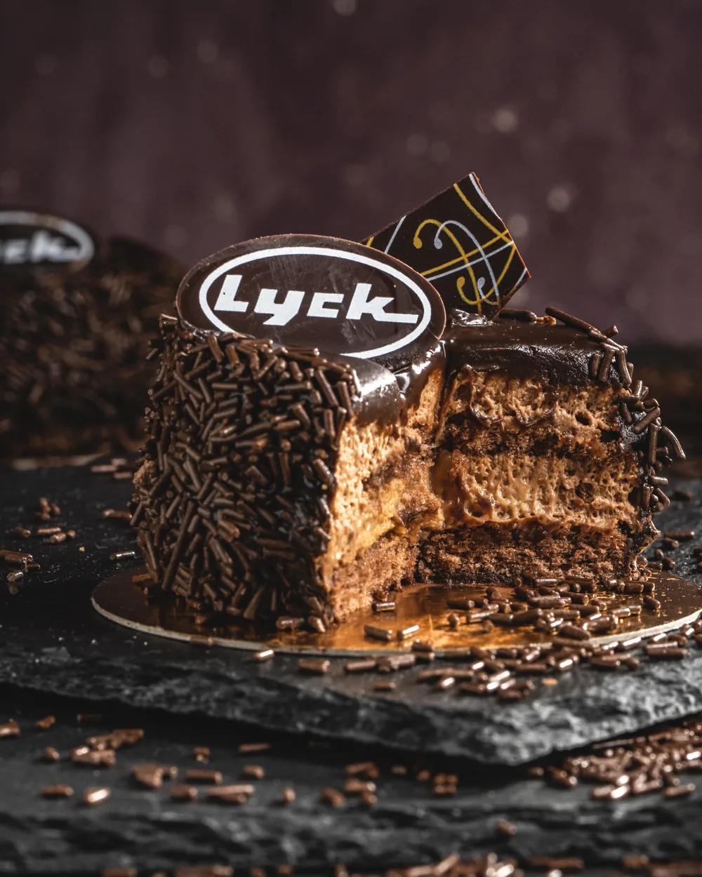 Ein angeschnittenes Schokoladentörtchen mit Lyck-Plakette, im Anschnitt die Schichten aus Creme und Biskuit.