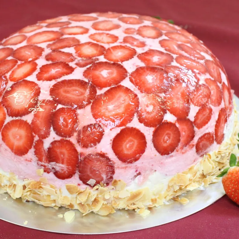 Eine hohe Torte, dicht mit halbierten Erdbeeren bedeckt, darunter rosa Sahne.