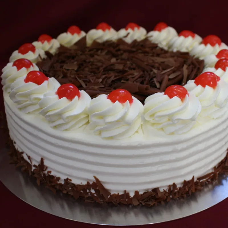 Eine Sahnetorte mit Schokoraspeln in der Mitte, am Rand Sahnetupfer mit je einer Kirsche.