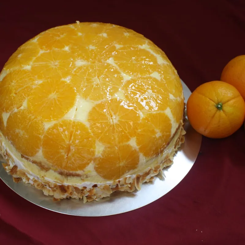 Eine gewölbte Torte, vollständig mit Mandarinenspalten bedeckt, am Rand Mandelblättchen.