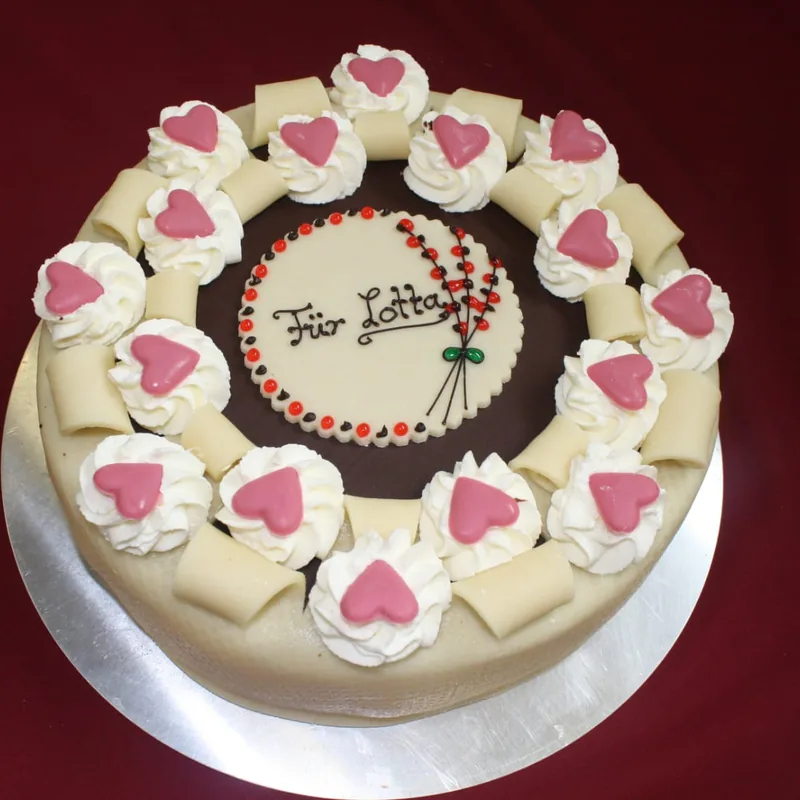 Eine Motivtorte mit weißer Abdeckung, aufgelegten Herzen am Rand und einem Schriftzug in der Mitte.