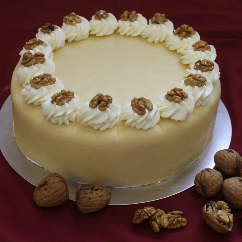 Eine hell glasierte Torte mit einem Kranz aus Sahnetupfern, auf jedem eine Walnusshälfte.