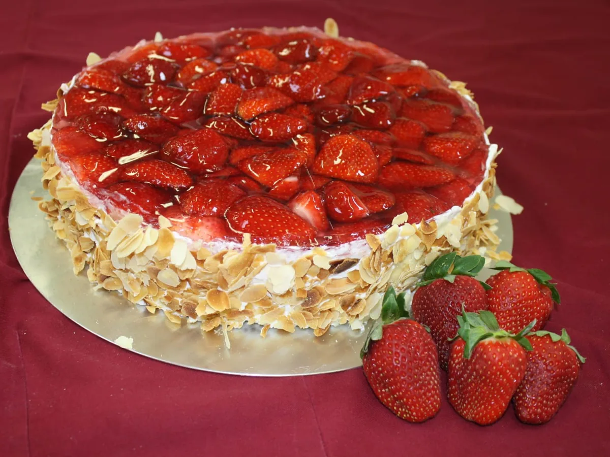 Eine Sahnetorte, mit halbierten Erdbeeren belegt und mit Mandelblättchen am Rand.